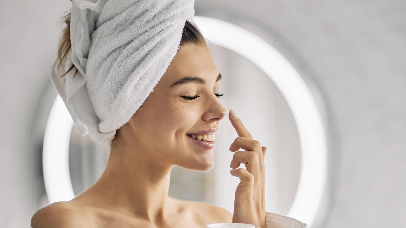 Frau im Bademantel mit Handtuchturban tupft sich Creme auf die Nase